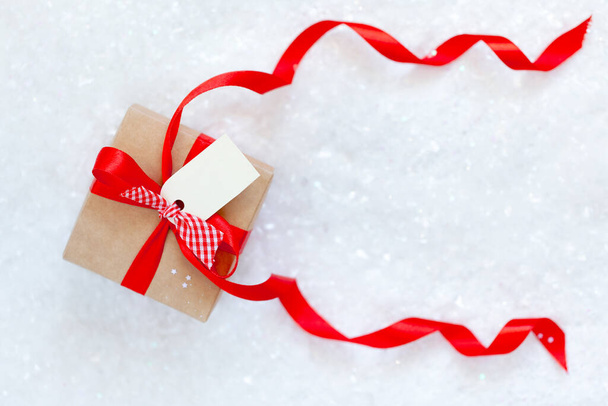 Coffret cadeau festif avec arc rouge et étiquette vide pour le texte. Noël présent dans la neige, à plat. Concept vacances et Nouvel An. - Photo, image