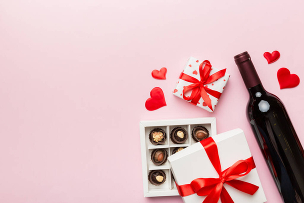 Bottle of red wine on colored background for Valentine Day with gift and chocolate. Heart shaped with gift box of chocolates top view with copy space. - Photo, Image