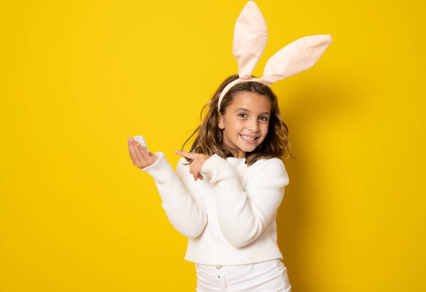 Портрет милої маленької дівчинки з вухами кролика та великодніми яйцями ізольовані на жовтому тлі
. - Фото, зображення