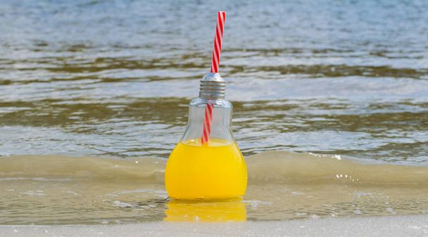 Fresh, lemonade or cocktail in a glass bottle with a straw close-up on the beach sand near the water. Travel and recreation concept - 写真・画像