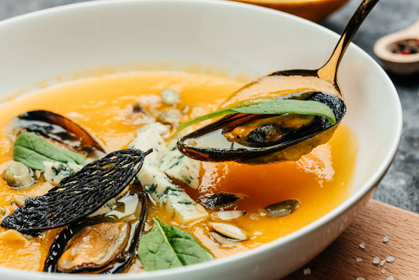 Тыквенный традиционный суп с морепродуктами, мидиями, креветками, голубым сыром, плесенью в белой миске. Фон рецепта еды. Закрыть. - Фото, изображение