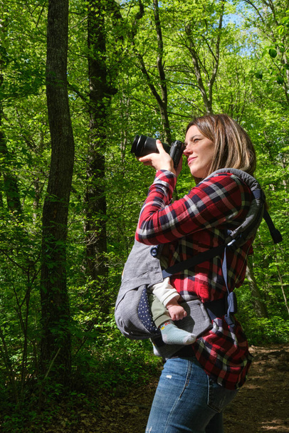 Mulher branca com câmera, fotografando a floresta com um bebê em um carrinho de bebê. - Foto, Imagem