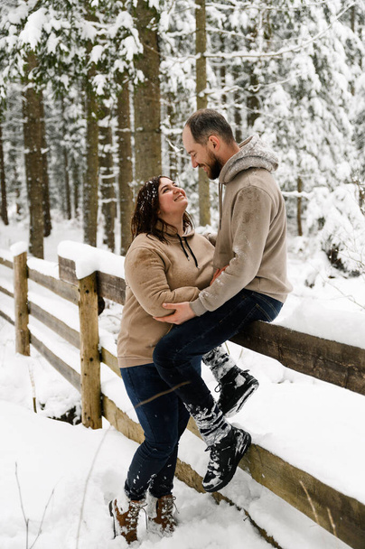 Walk in winter. Embracing couple enjoying snowfall. Man and woman having fun in the frosty forest. Romantic date in winter time.Christmas mood of a young family. Love and leisure concept - Photo, Image