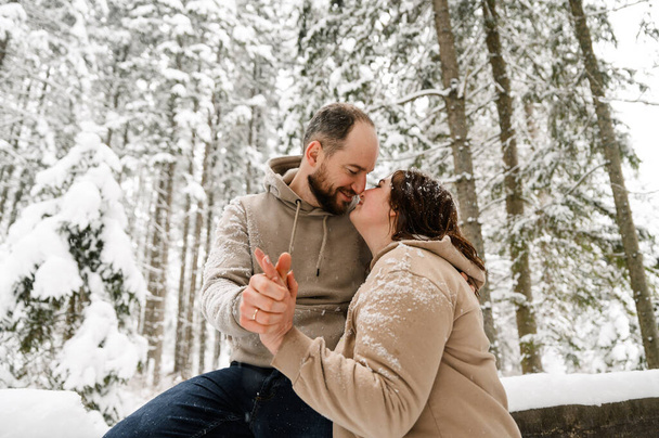 Walk in winter. Embracing couple enjoying snowfall. Man and woman having fun in the frosty forest. Romantic date in winter time.Christmas mood of a young family. Love and leisure concept - 写真・画像