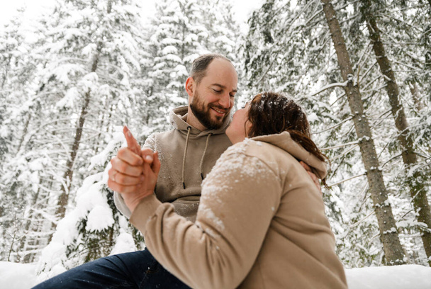 Walk in winter. Embracing couple enjoying snowfall. Man and woman having fun in the frosty forest. Romantic date in winter time.Christmas mood of a young family. Love and leisure concept - Foto, afbeelding
