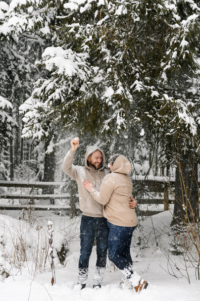 Wandern im Winter. Umarmendes Paar genießt den Schneefall. Mann und Frau amüsieren sich im frostigen Wald. Romantisches Date in der Winterzeit. Weihnachtsstimmung einer jungen Familie. Liebe und Freizeitkonzept - Foto, Bild