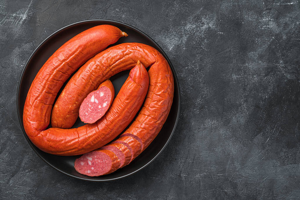 A plate of smoked sausage with sliced pieces on a dark background. Top view, copy space. - Photo, Image