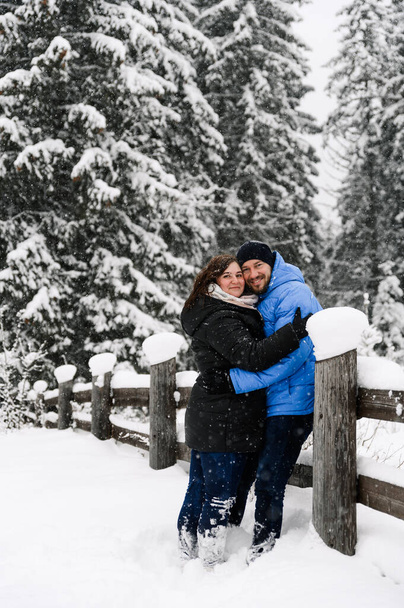 Walk in winter. Embracing couple enjoying snowfall. Man and woman having fun in the frosty forest. Romantic date in winter time.Christmas mood of a young family.  Love and leisure concept - Photo, image