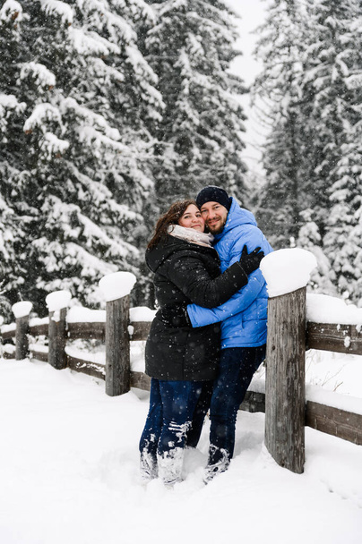 Walk in winter. Embracing couple enjoying snowfall. Man and woman having fun in the frosty forest. Romantic date in winter time.Christmas mood of a young family.  Love and leisure concept - Foto, Bild