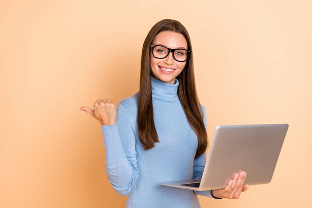 Photo of smart brunette young lady hold laptop index promo wear spectacles blue turtleneck isolated on beige color background - Fotoğraf, Görsel