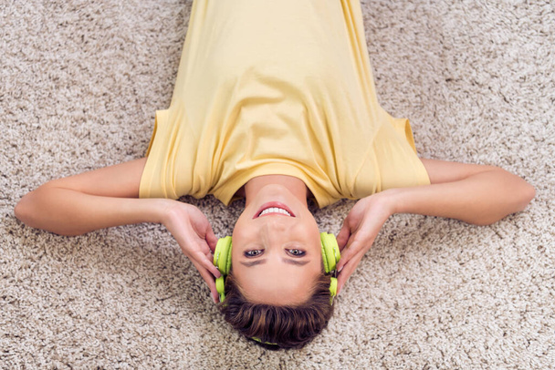 High angle photo of dreamy adorable young woman dressed yellow t-shirt lying floor listening music smiling indoors home room - Foto, Imagem