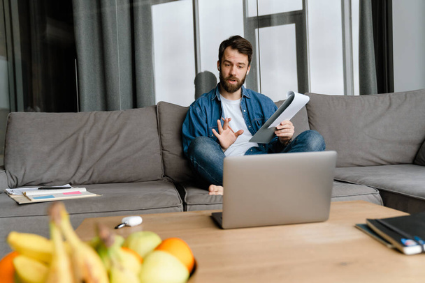 Bearded european man working with laptop while sitting on sofa at home - Foto, imagen