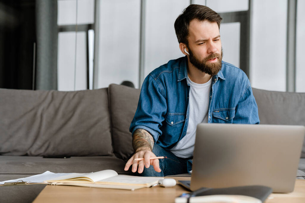 Bearded european man working with laptop while sitting on sofa at home - Φωτογραφία, εικόνα