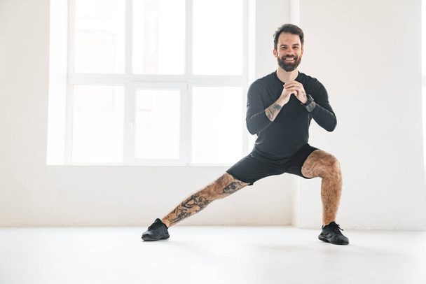 Smiling mid aged white sportsman exercising in a bright room doing lunges - Foto, Imagen