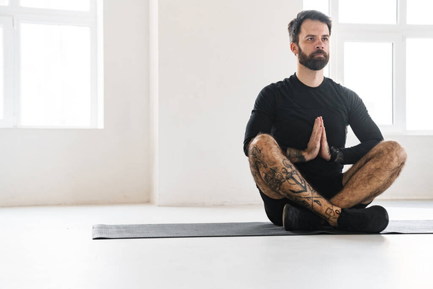 Bearded sportsman with tattoo doing exercise during yoga practice indoors - Foto, Imagen