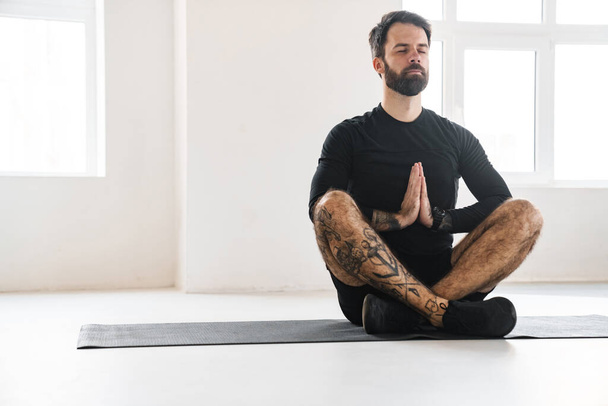 Bearded sportsman with tattoo meditating during yoga practice indoors - Foto, Bild