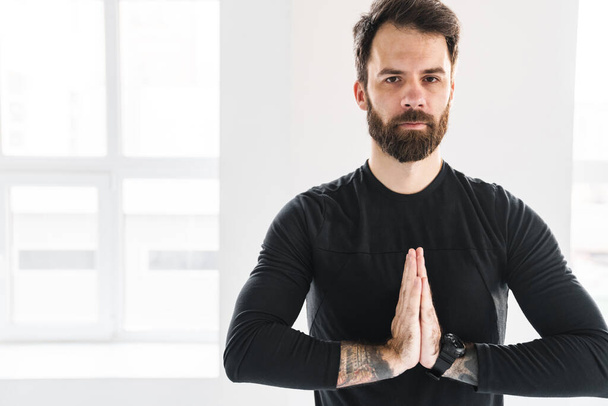 Bearded sportsman with tattoo meditating during yoga practice indoors - Foto, afbeelding