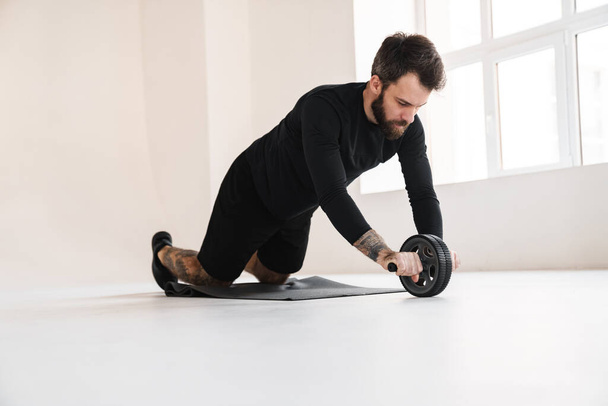 Young healthy brunette sportsman exercising on a fitness mat with roller indoors - Фото, зображення
