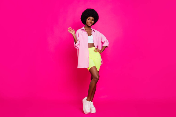 Photo of sweet charming dark skin woman dressed crop top smiling waving arm isolated pink color background - Фото, изображение