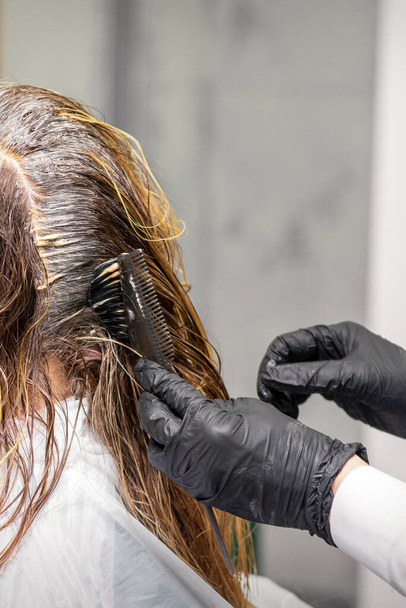 Um cabeleireiro em luvas pretas está aplicando a cor da escova no cabelo de um cliente. Coloração do cabelo em um salão de beleza close-up - Foto, Imagem