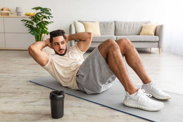 Атлетический араб тысячелетия делает упражнения на коврике для йоги, укрепляет мышцы пресса дома, полная длина - Фото, изображение