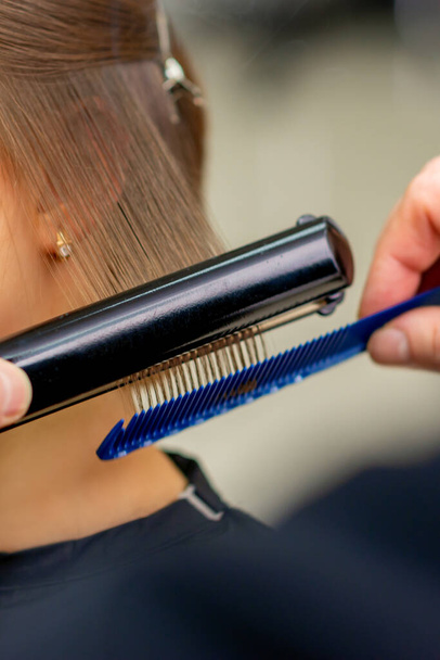 Перукарня випрямляє волосся молодої брюнетки в салоні краси
 - Фото, зображення