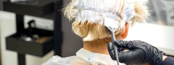 Η επαγγελματίας κομμώτρια βάφει τα μαλλιά της πελάτισσάς της σε σαλόνι ομορφιάς. - Φωτογραφία, εικόνα