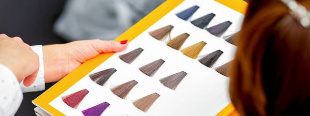 Young caucasian woman choosing a color from the hair color chart in a beauty salon - 写真・画像