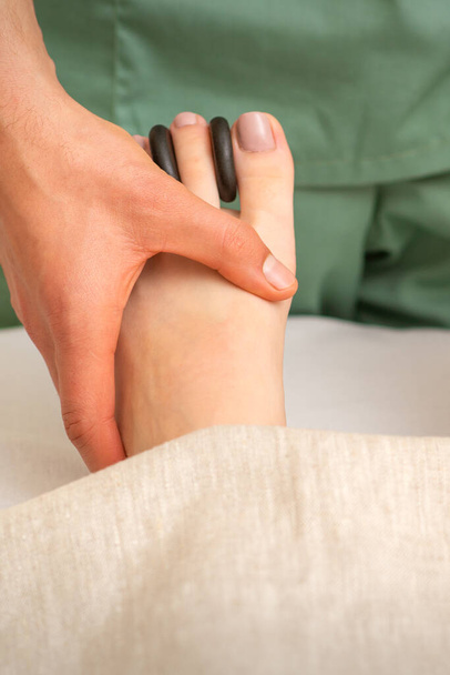 Masseur faisant massage des pieds et des orteils avec des roches entre les orteils d'une femme - Photo, image