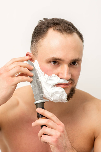 Jovem caucasiano barba barbear homem com uma grande faca no fundo branco - Foto, Imagem