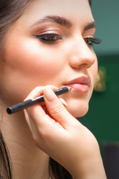 Maskenbildner oder Kosmetikerin bemalt Konturlippen einer jungen Frau mit einem Bleistift in Nahaufnahme - Foto, Bild