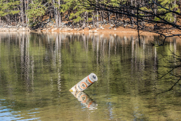 Broken and cracked no wake buoy floating on its side a warning to go slow in shallow water in the inlet of the lake with the shoreline in the background on a sunny day - Photo, Image