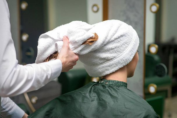 Ein Friseur wickelt die nassen Haare der jungen Frau nach dem Waschen im Schönheitssalon in ein Handtuch - Foto, Bild