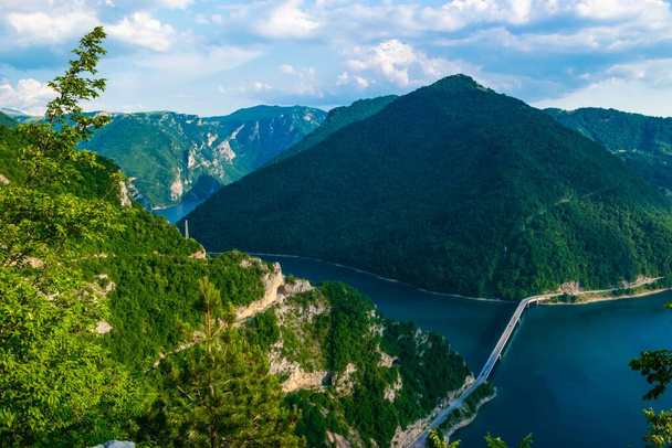 Brücke über den Piva-See in einer Schlucht zwischen hohen grünen Bergen bei Pluzine. Sommerlandschaft. Nordmontenegro. Schöne Natur des Balkans. - Foto, Bild