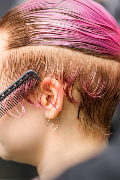 Расчесывание волос молодой женщины во время окрашивания волос розовым цветом в парикмахерской крупным планом - Фото, изображение