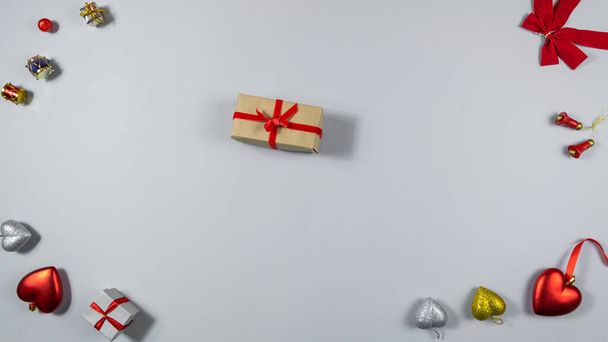 Gift box tied with red ribbon in festive frame on light gray background. Red hearts, bow and other decorations with copy space in center. Concept of holidays and gifts. Flat lay. Copy space. - Foto, Imagen