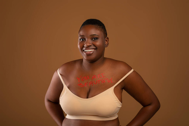 Curvy χαμογελώντας μαύρη γυναίκα ποζάρει με επιγραφή στο στήθος της - Φωτογραφία, εικόνα