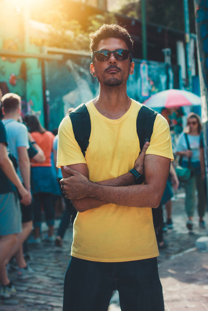 Przystojny Czarny Mężczyzna w żółtej koszuli i okularach na tle ulicy Ludzie zdezorientowani. - Zdjęcie, obraz