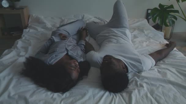 Onnellinen afrikkalainen amerikkalainen rakastava pari pyjamassa rentouttava sängyssä, kädestä pitäminen ja nauraminen, harrastus yhdessä - Materiaali, video