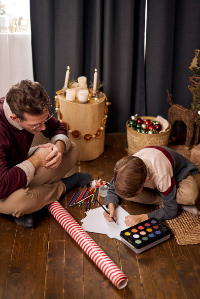 Child boy preparing christmas surprise for beloved people , sit on floor drawing - Photo, Image