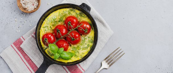 Frittata with arugula, potatoes and cherry tomatoes in iron pan on old stone table background. Top view. - 写真・画像