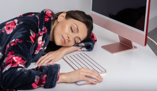 Уилтшир, Великобритания. 2021 год. Женщина, работающая из дома, спит за компьютером и клавиатурой.  - Фото, изображение