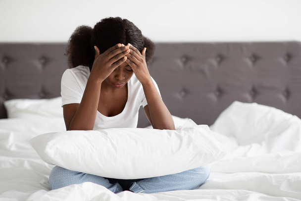 Overstuur zwarte vrouw zitten in bed en aanraken van haar hoofd - Foto, afbeelding