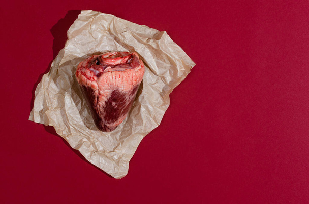 Top view of real animal heart on a piece of craft paper and red background. - Foto, Bild