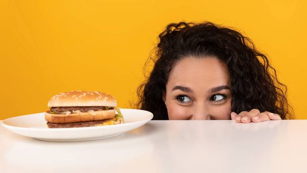 空腹の女性はハンバーガーのテーブルをのぞき見見て - 写真・画像