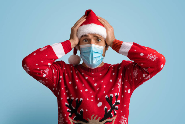 Christmas Lockdown. Shocked Young Man Wearing Santa Hat And Medical Face Mask - Fotoğraf, Görsel