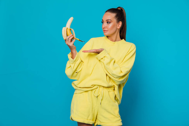 woman in yellow clothes with banana fruit on a blue background - Foto, afbeelding
