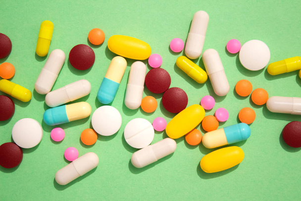 Detailní záběr pestrobarevných lékových pilulek, tobolek a tablet na zeleném pozadí. Vitamíny a suplemity imunitního systému. Různé doplňky stravy. Selektivní zaměření - Fotografie, Obrázek