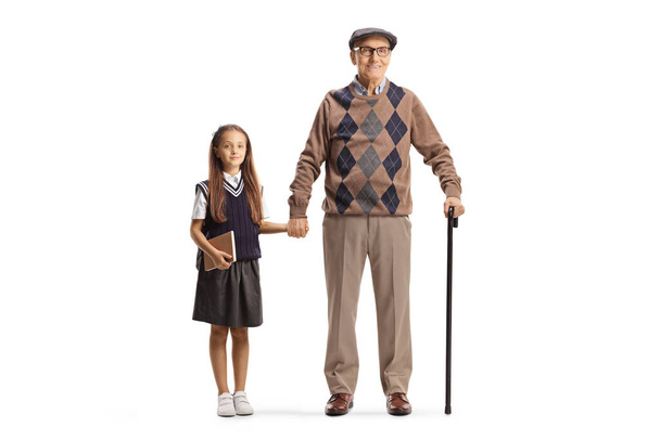 Full length portrait of a grandfather and granddaughter schoolgirl standing and holding hands isolated on white background - 写真・画像