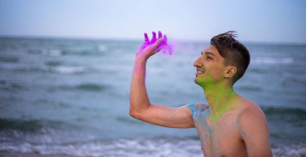A young guy throws colour powder against the background of the sea - Fotoğraf, Görsel